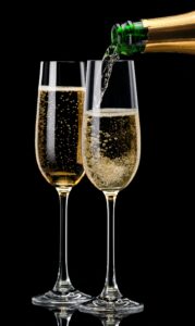 two champagne glasses being filled from the bottle against a black backgroun