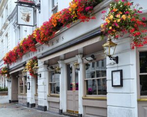 Profuse baskets of red flowers hanging from the first floor of the Hereford Arms pub, which is white